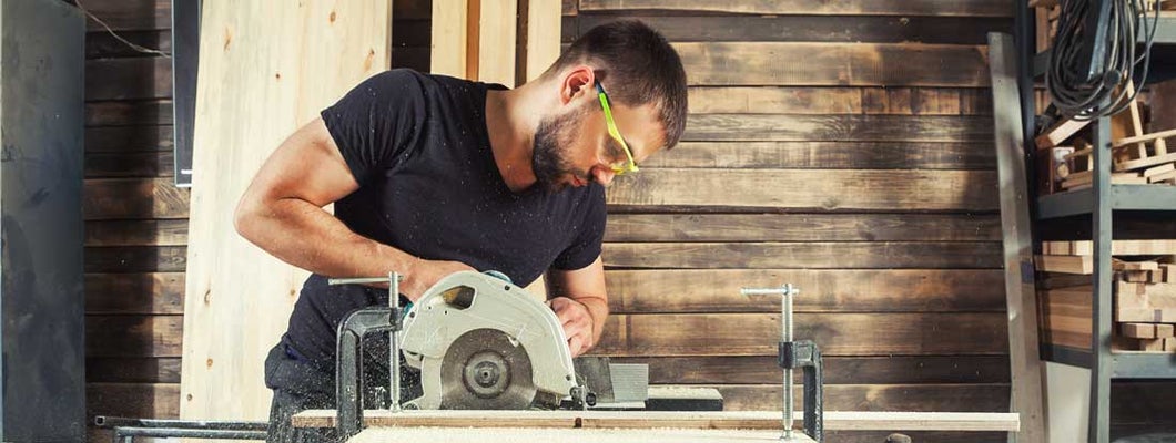 A man builder saws a board with a circular saw in the workshop