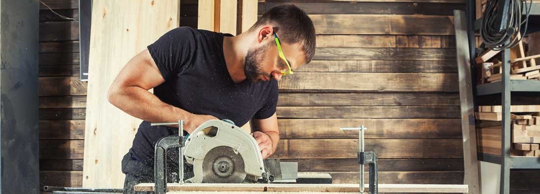 A man builder saws a board with a circular saw in the workshop. Find Carpenter Liability Insurance.