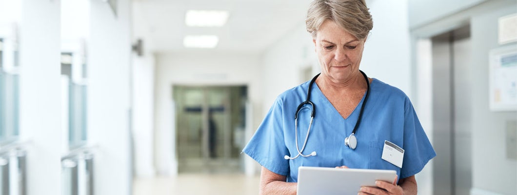 Female nurse using a tablet while standing in the hospital corridor. Find Nursing Malpractice Insurance.