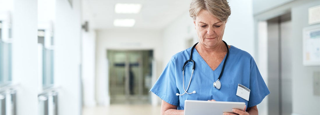 Female nurse using a tablet while standing in the hospital corridor. Find Nursing Malpractice Insurance.