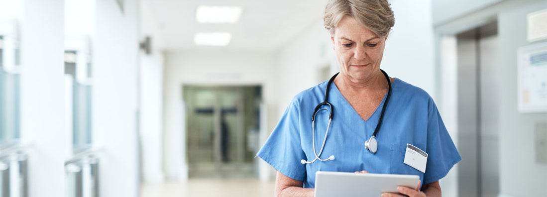 Female nurse using a tablet while standing in the hospital corridor. Find Nurse Insurance.