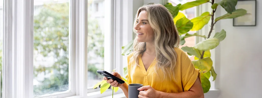 Woman in her condo using her cell phone while drinking coffee. Find Missouri Condo Insurance.