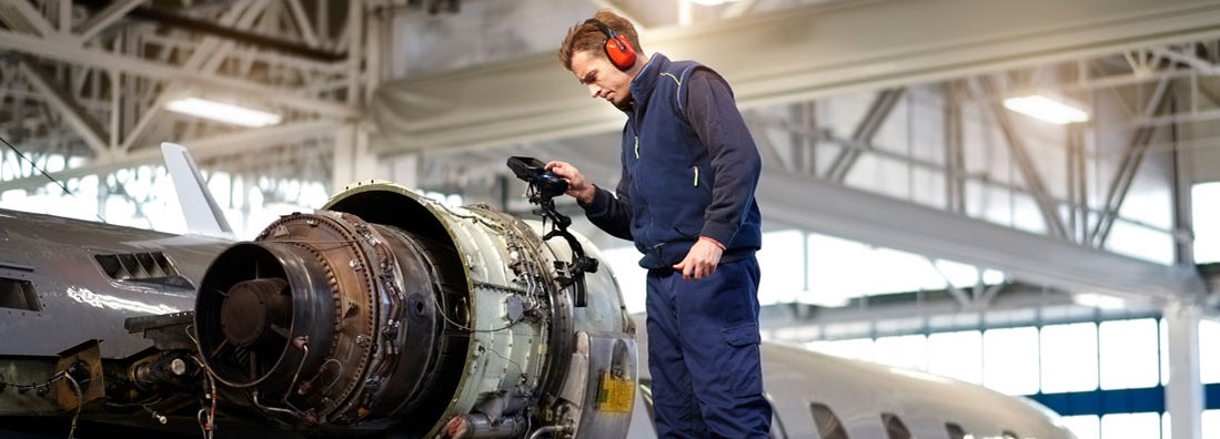 Aircraft engineer in the hangar repairing and maintaining airplane jet engine.