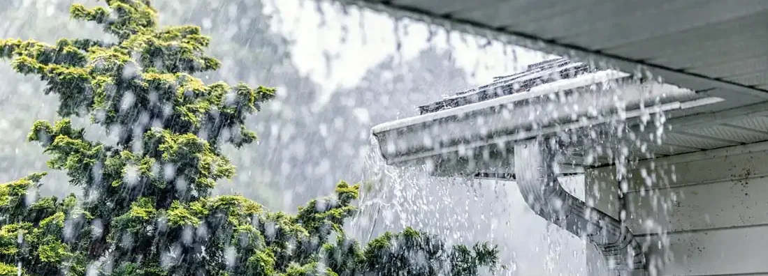 Downpour rain splashing over the edge of the tile shingle roof during a torrential mid-summer storm. Find Homeowners Hazard Insurance.