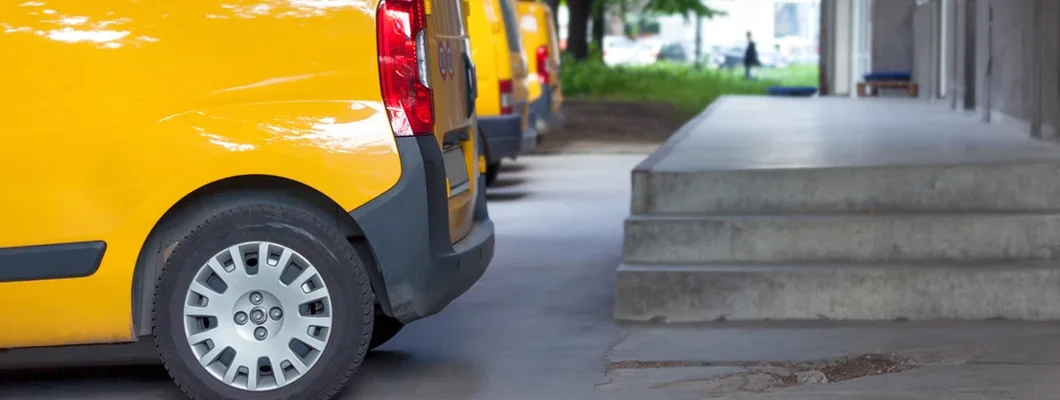 Side view of yellow delivery vans parked in front on the entrance a warehouse at distribution center. Find Delaware Commercial Vehicle Insurance.