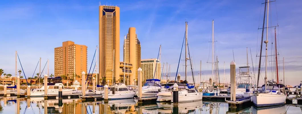 Towers along Corpus Christi , TX at sunrise with a reflecting cityscape painted at golden hour. Find Texas Boat Insurance.