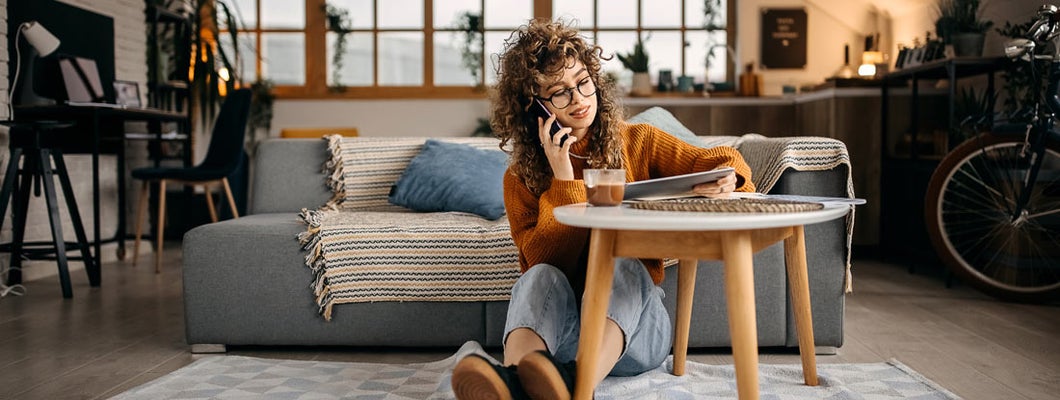 Young woman sitting on a floor and talking on a mobile phone. Find Delaware renters insurance.