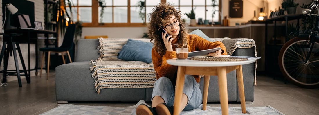 Young woman sitting on a floor and talking on a mobile phone. Find Delaware renters insurance.