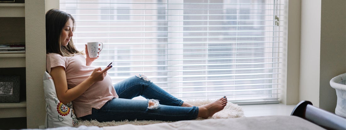Smiling pregnant woman using her smartphone at home