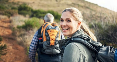 Portrait of a mature woman hiking with her husband through the mountains. Whole Life vs Term Life Insurance.