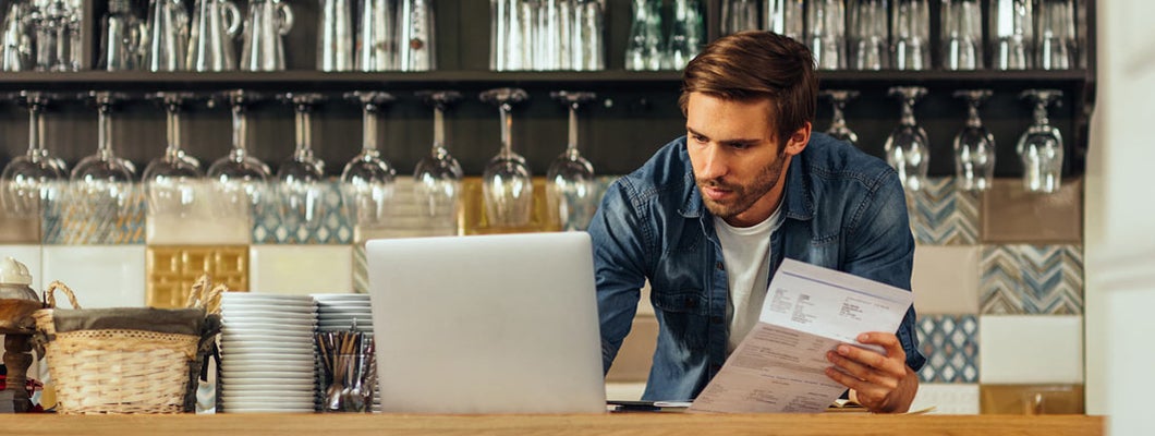 Male cafe owner standing at the counter and paying. Thirteen Business Insurance Pitfalls to Avoid. 