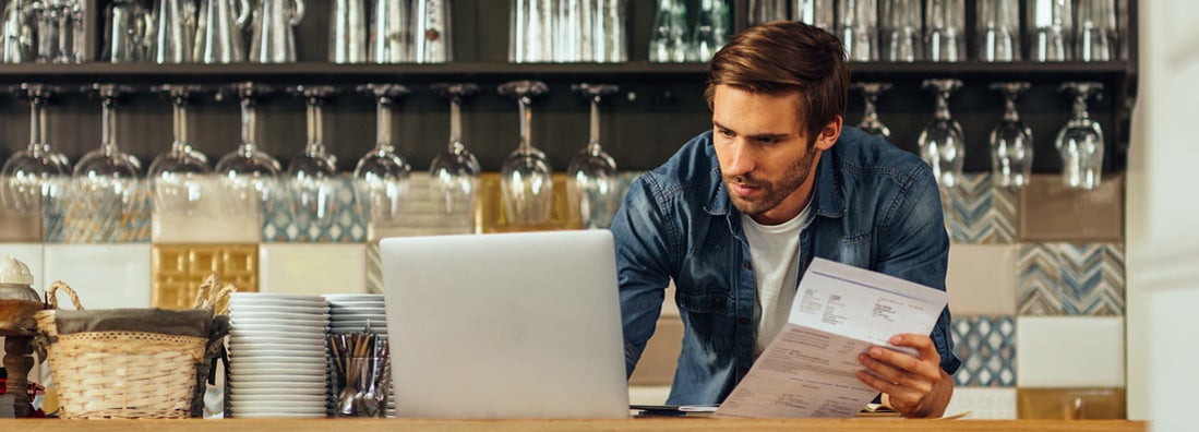 Male cafe owner standing at the counter and paying. Thirteen Business Insurance Pitfalls to Avoid. 