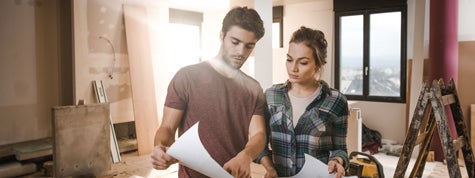 Young couple examining blueprints while being on construction site in their home
