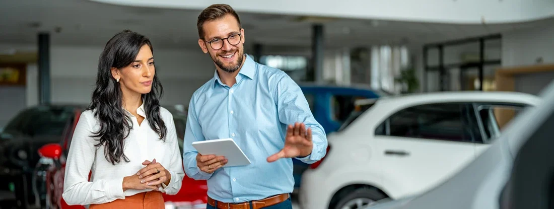 Happy salesman selling the car to his female customer in a showroom. 10 Car Buying Secrets You Need to Know.