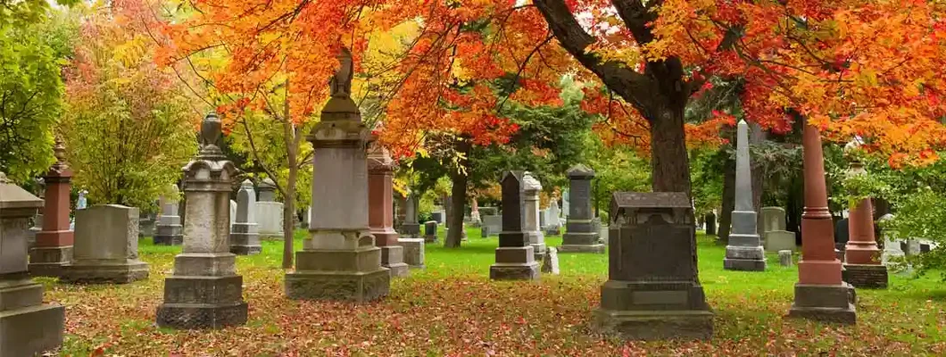 Grave stones and memorials under a red maple tree. Find Cemetery Insurance.