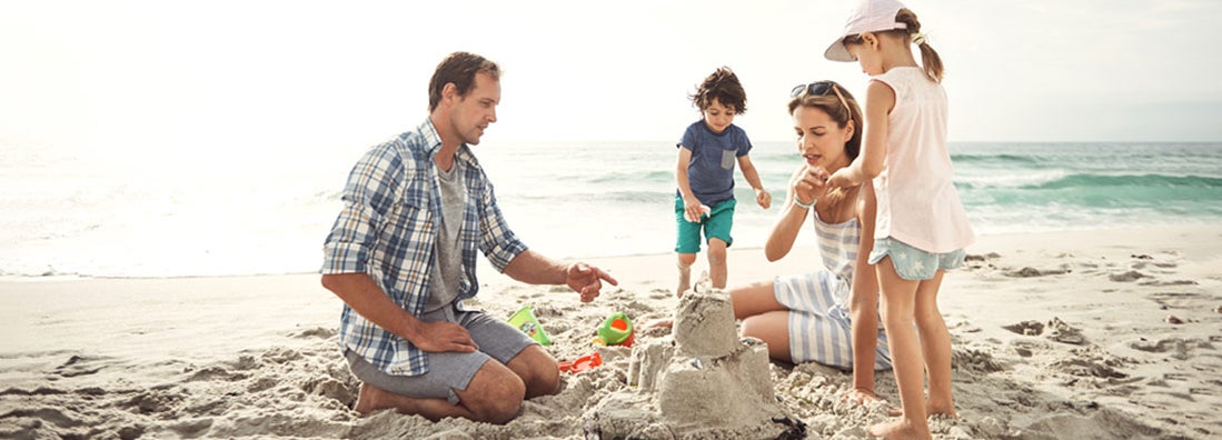 Family with young children building a sandcastle together on the beach