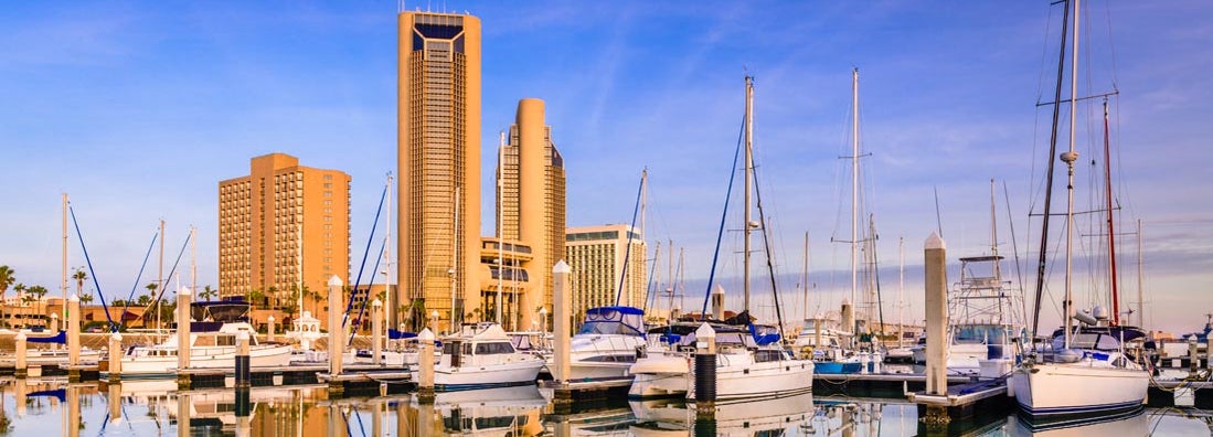 Towers along Corpus Christi , TX at sunrise with a reflecting cityscape painted at golden hour. Find Texas Boat Insurance.