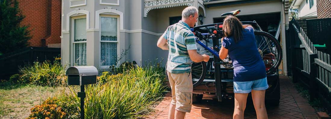 Middle aged couple in driveway attaching the family bikes to the bicycle rack on their car. Find Florida personal umbrella insurance.