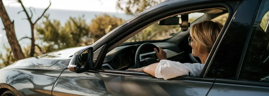 Woman sitting in her car and looking at a beautiful lake. The best cars and SUVs for people with bad backs.