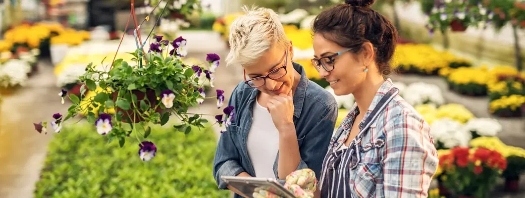 Florist woman showing a list of flowers on a tablet to the curious female customer in a greenhouse. Find BOP Insurance. 