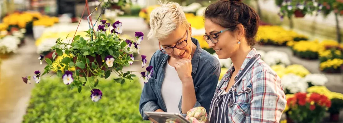 Florist woman showing a list of flowers on a tablet to the curious female customer in a greenhouse. Find BOP Insurance. 