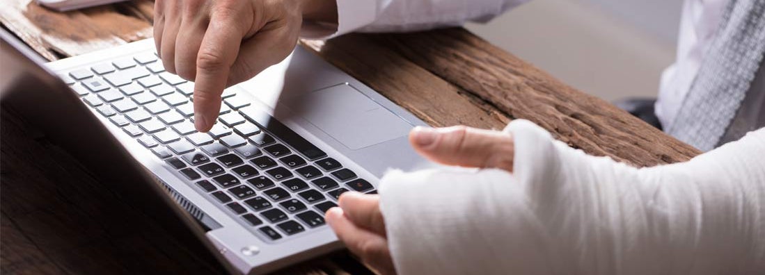 Businessperson With Hand Injury Using Laptop. How to Implement a Return to Work Policy.