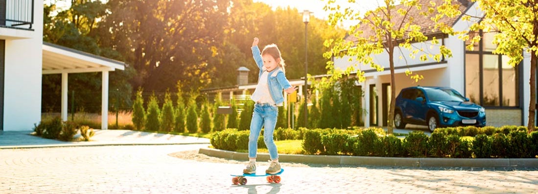 Little girl outdoors near house and car riding skateboard. Find Washington umbrella insurance.