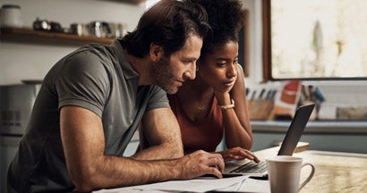 Couple using a laptop while doing their budget paperwork in their kitchen at home. 10 things to know about renewing insurance. 