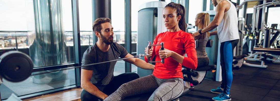 Workout with personal trainer on rowing machine at gym. Find Personal Trainer Insurance.
