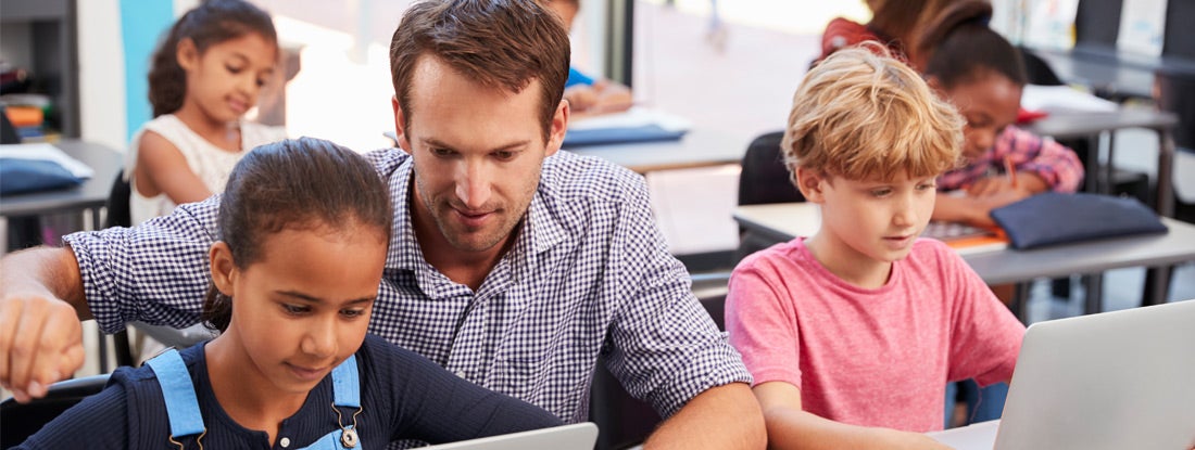 Teacher helping young students using laptops in class