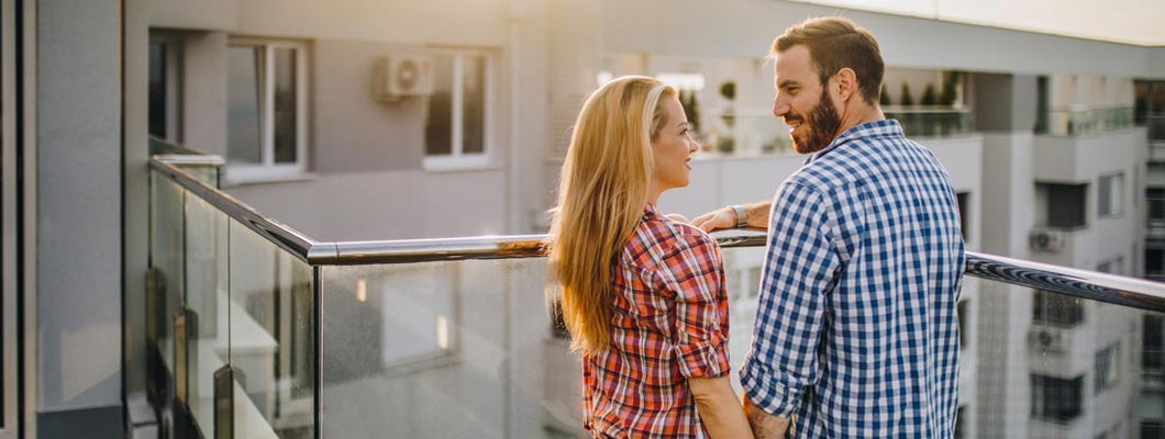 Young couple holding hands and talking on a condominium terrace. Find Washington condo insurance.