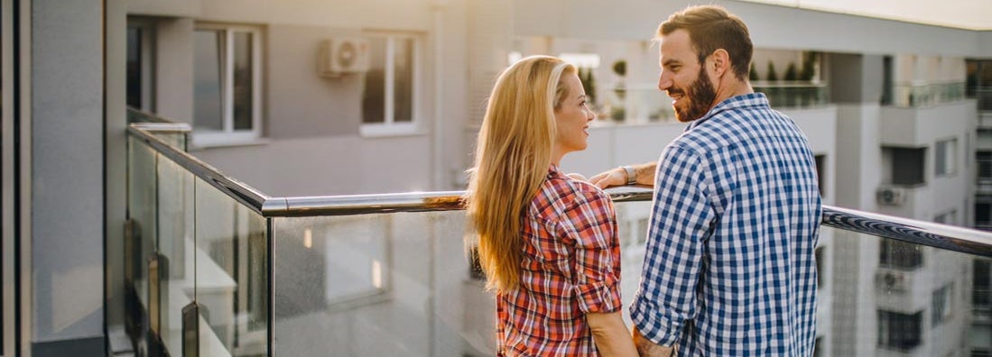 Young couple holding hands and talking on a condominium terrace. Find Washington condo insurance.