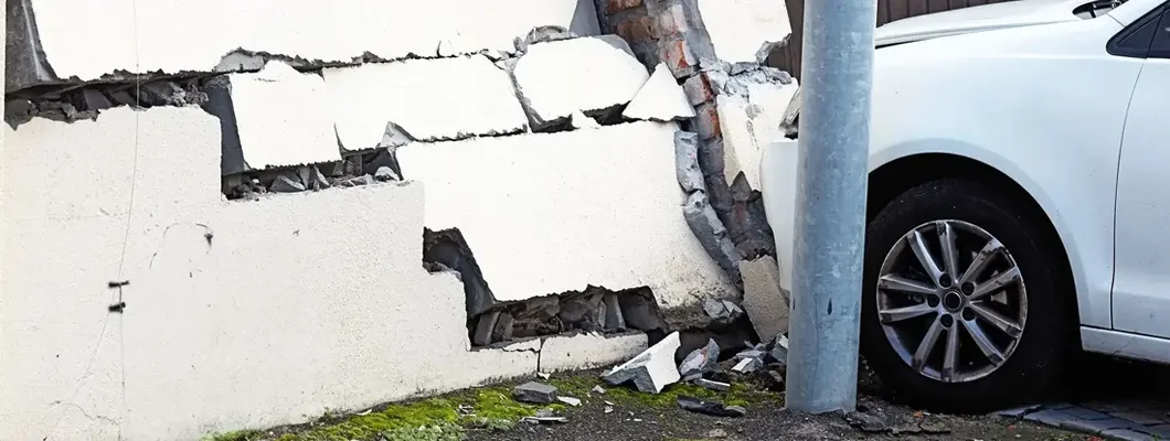 Smashed wall and damaged car in the aftermath of a traffic accident. Car damage to property.