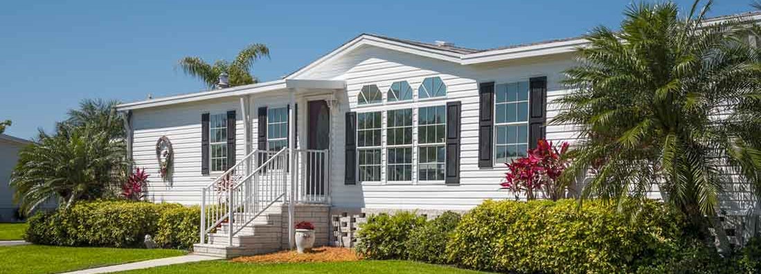 Mobile home landscaped with front lawn, palm trees and a clear sky. How mobile homes are insured.