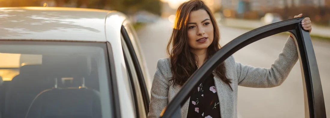 Beautiful young woman getting out of car in the city at sunset. Car Insurance in Montpelier, Vermont.