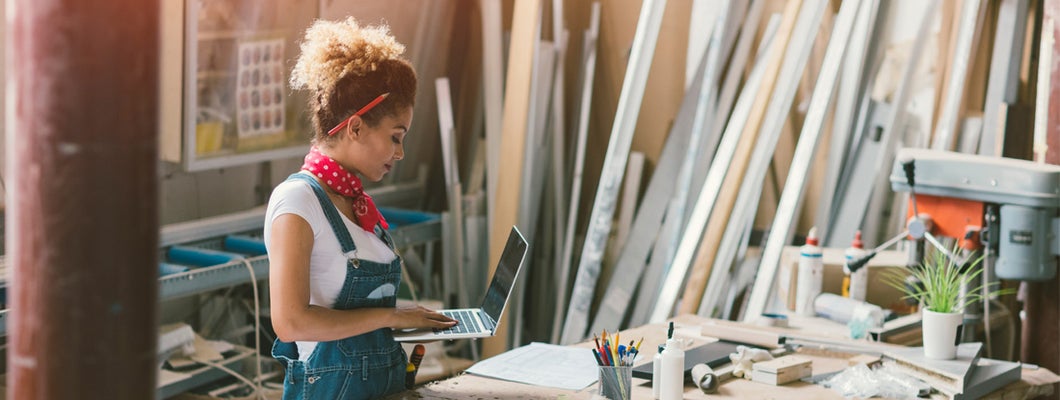 Carpenter standing in her workshop. Holding laptop while she focused on her work.