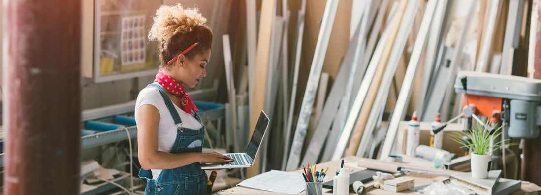 Carpenter standing in her workshop. Holding laptop while she focused on her work.