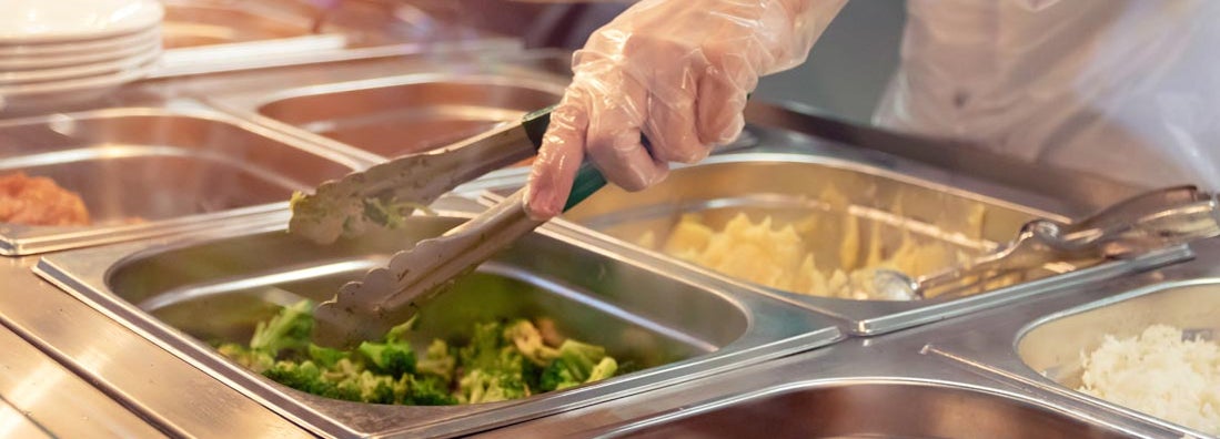 Chef standing behind full lunch service station with assortment of food in trays.
