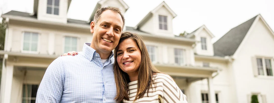 What Does Homeowners Insurance Cover? 2026 Guide. Portrait of married couple standing in front of suburban home.