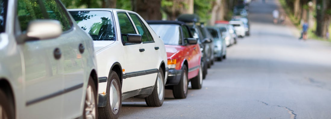 Street with long row of cars parked along a tree avenue