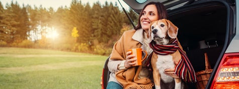 Woman and dog sit together in car trunk in autumn