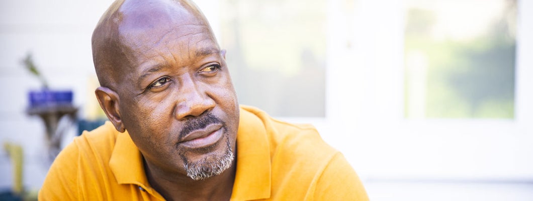 Mature man looks out while standing on his porch. Find a life insurance policy.