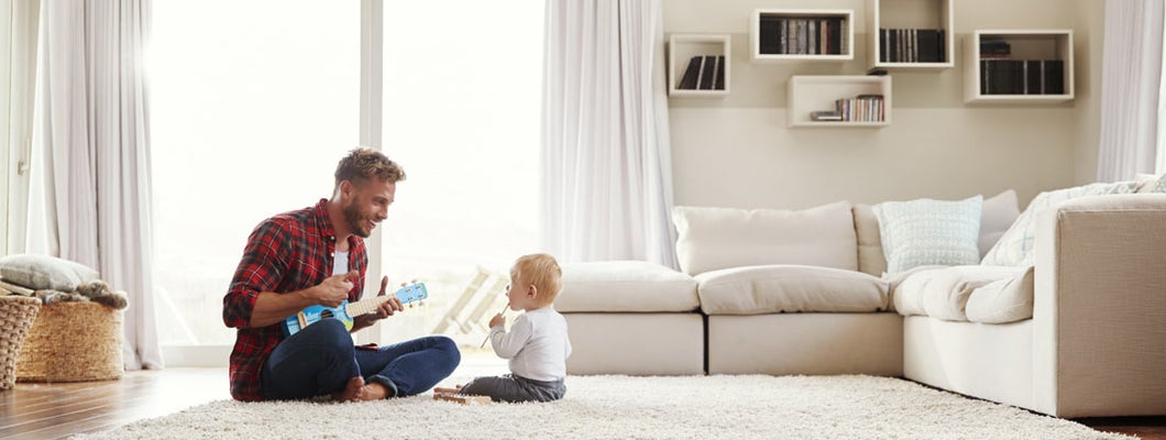 Father playing ukulele with young son in their sitting room
