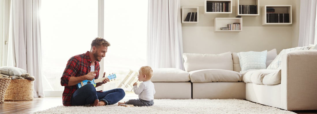 Father playing ukulele with young son in their sitting room