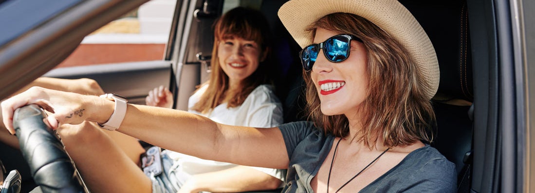 Woman in sunglasses and straw hat enjoying driving car with friend. Find Fort Myers Florida car insurance.