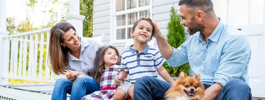 Happy family with two kids sitting in front of porch. Find Homeowners Liability Insurance.