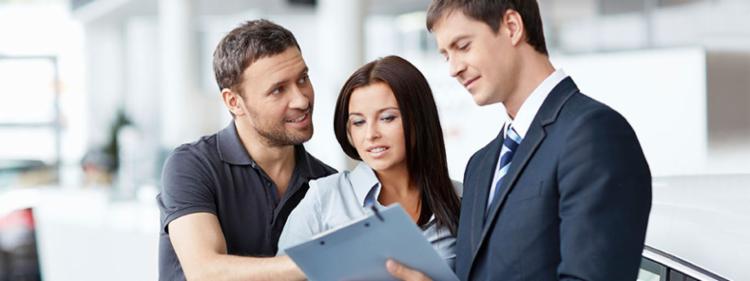 Couple negotiating paperwork with a car salesman.