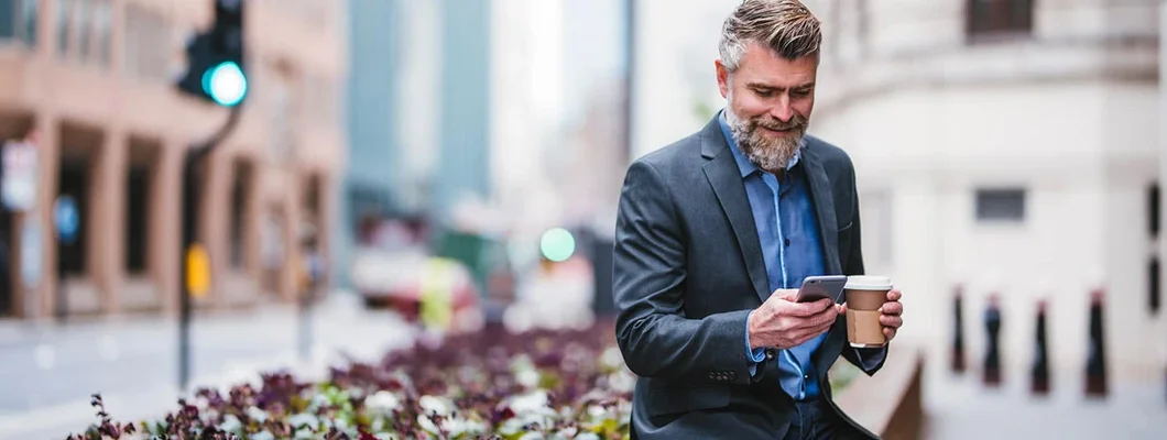 Businessman using mobile phone and holding coffee cup. Find North Carolina Landlord Insurance.