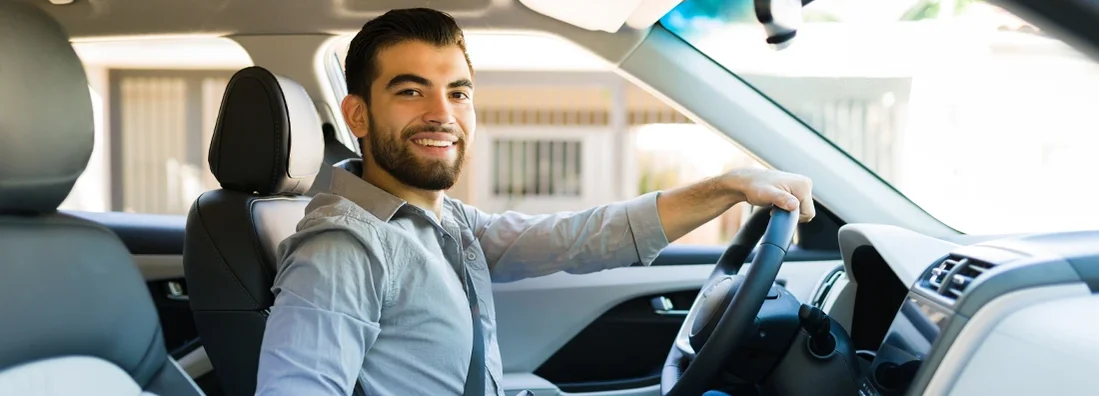 Hispanic man looking at the camera while driving his new car with pride. Cumberland Hill, Rhode Island Car Insurance.