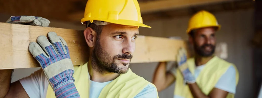 Manual workers carrying wood plank at construction site. Find Workers' Compensation Insurance for Contractors.